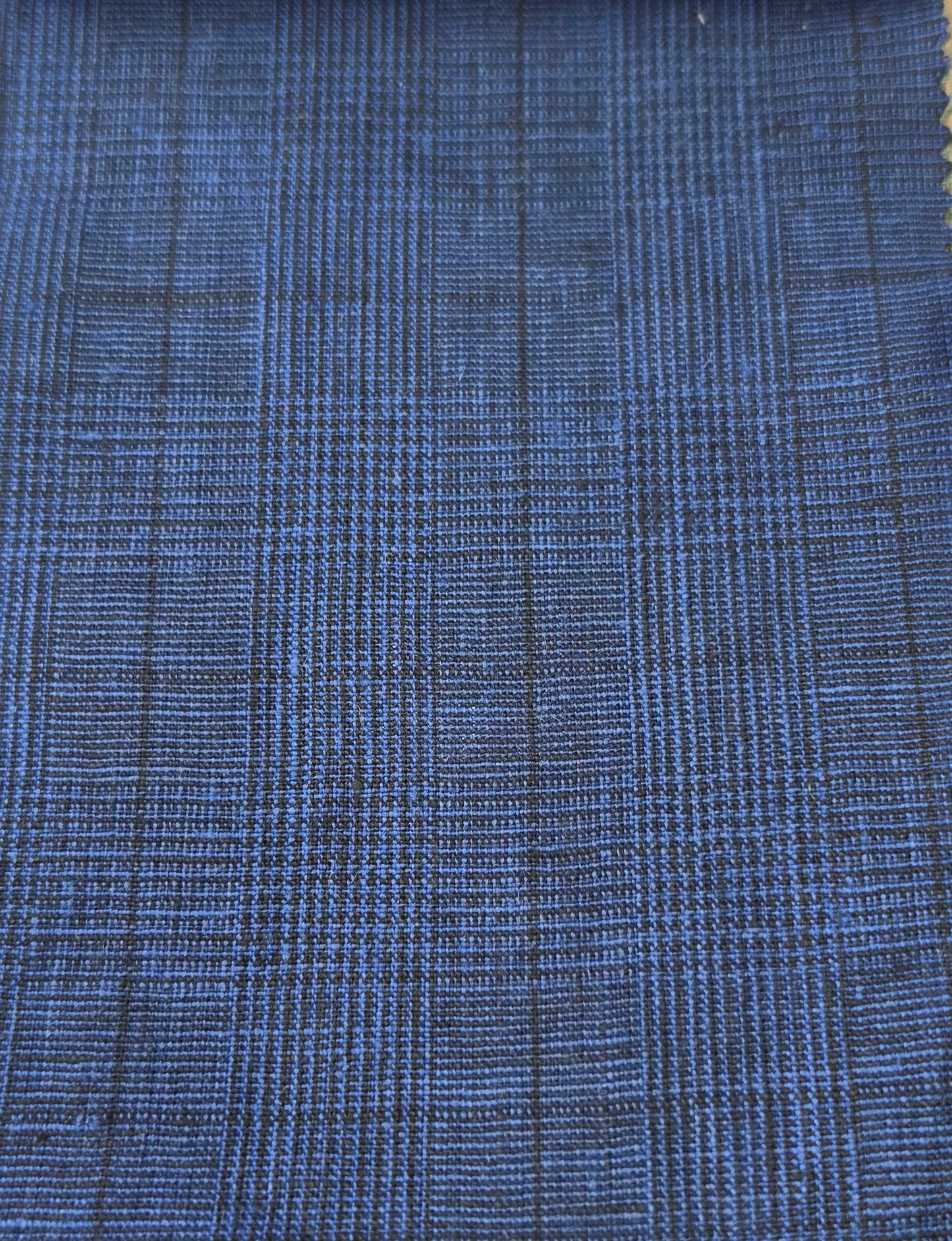 A close-up of a blue woven fabric with a subtle black plaid or grid pattern.