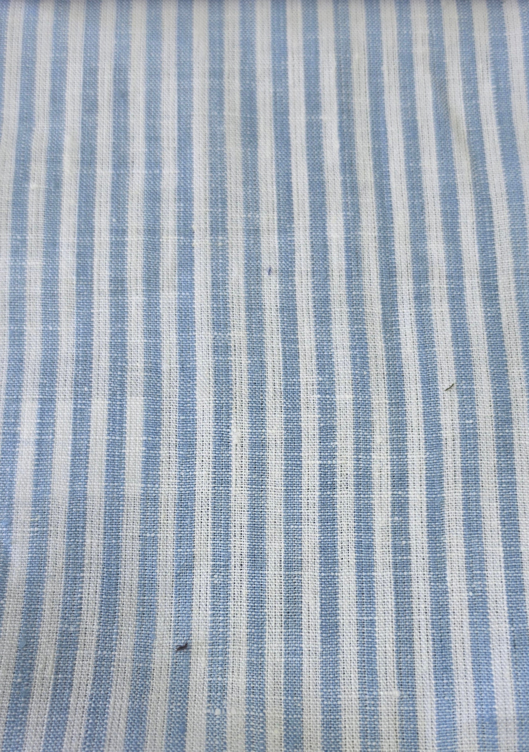 A close-up of a woven fabric with vertical stripes in light blue and off-white, showing a textured linen-like weave.