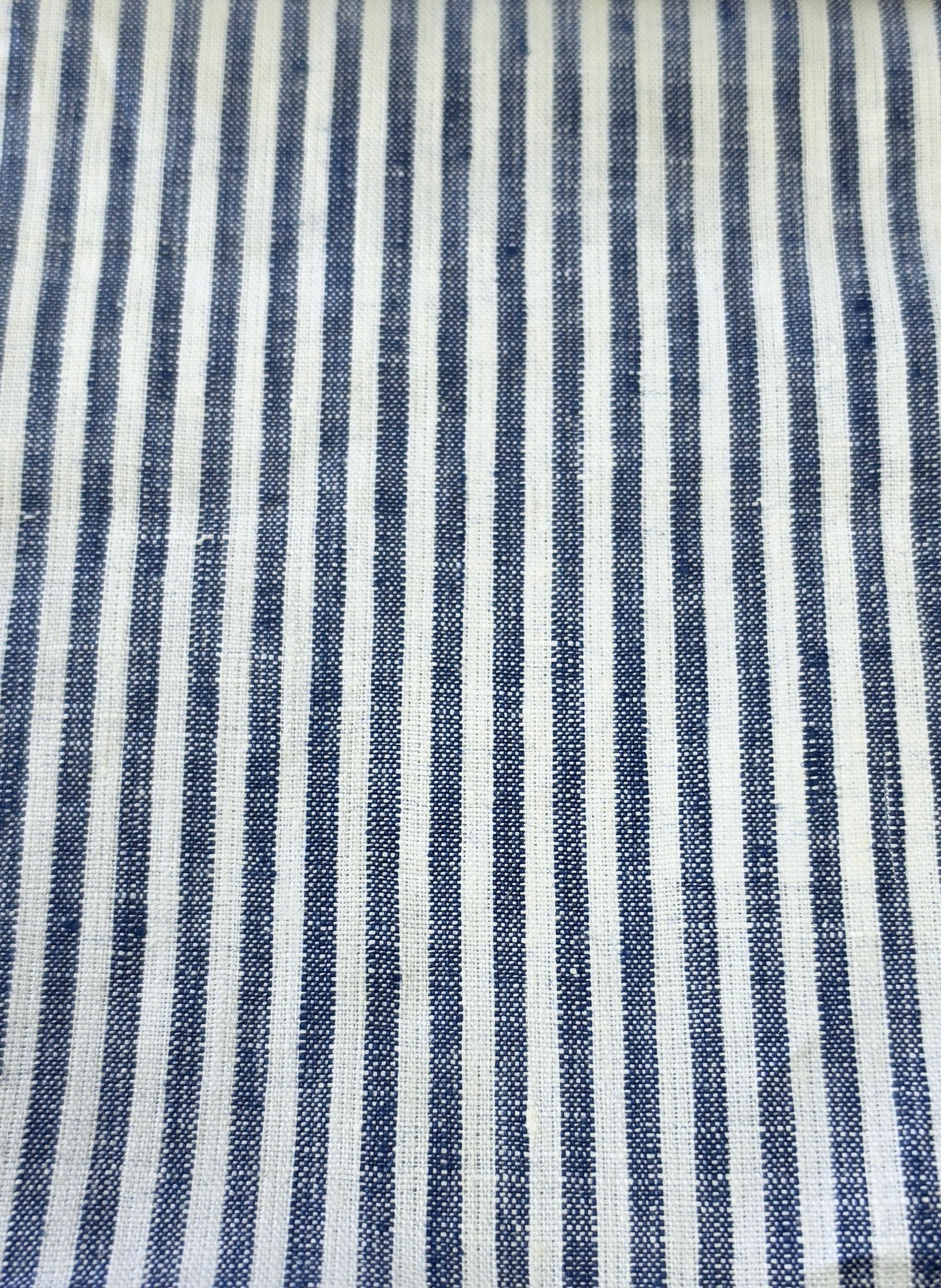A close-up of a woven fabric with vertical navy blue and off-white stripes, showing the textile texture.
