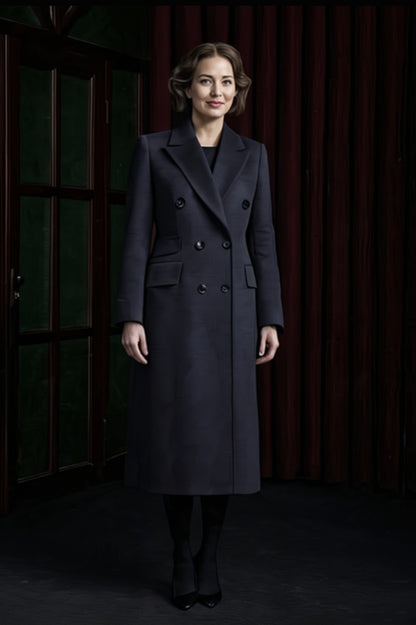 Woman wearing a dark coat standing against a dark background