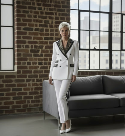 Lady in a white suit with black accents standing in a room with a brick wall and large window.