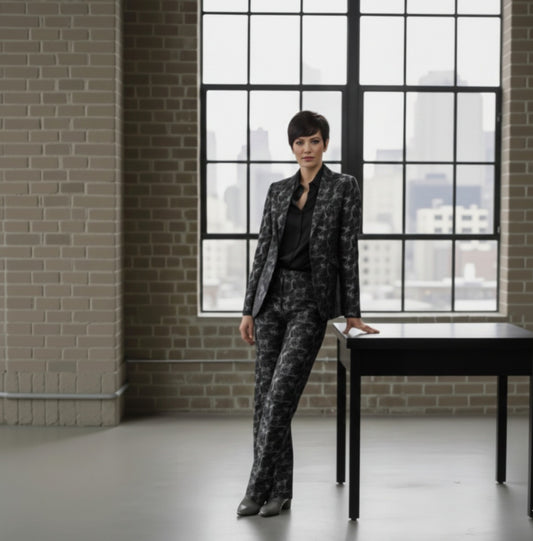 Lady wearing a patterned suit standing in a room with large windows and brick walls.