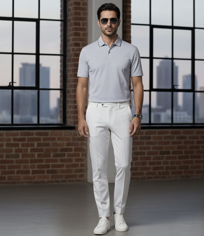 Man wearing a light Blue polo shirt and white pants standing in front of large windows with a cityscape view.