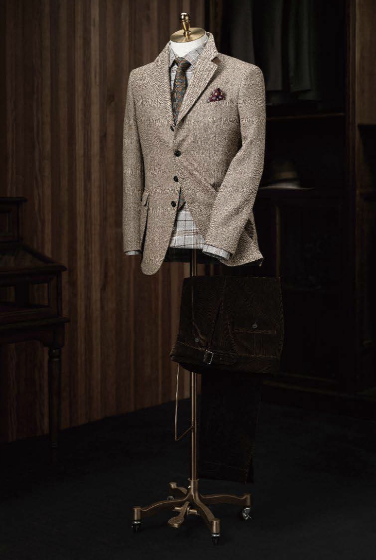 A light brown herringbone tweed jacket and green herringbone trousers displayed on a mannequin against a wooden background.