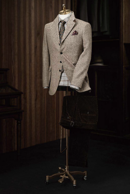 A light brown herringbone tweed jacket and green herringbone trousers displayed on a mannequin against a wooden background.