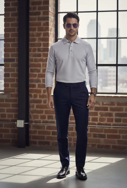 Man wearing a light gray long-sleeve polo shirt and dark blue pants standing in front of a brick wall with large windows.
