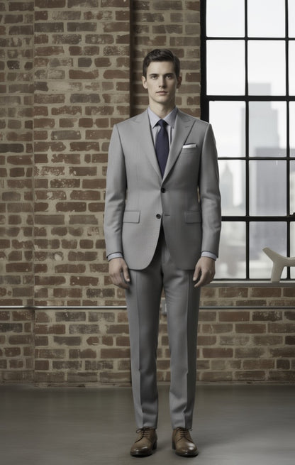Man wearing a light grey suit standing against a brick wall with a window in the background