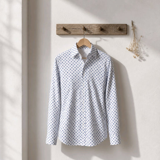 A light gray and white patterned long-sleeve button-up shirt hanging on a wooden hanger from a rustic wooden wall rack, set against a warm beige wall with soft window light shadows.