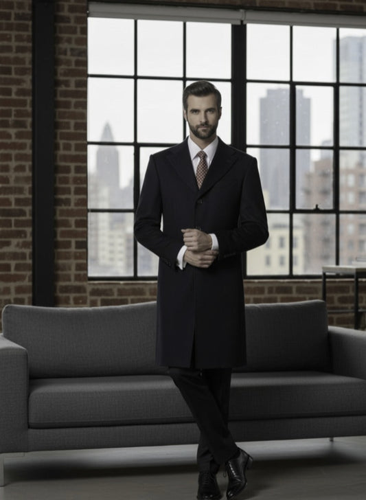 Man in a dark suit standing in a room with large windows and a gray sofa.