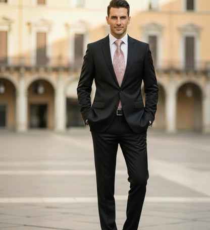 Man in a black suit with a pink tie standing in an open square with arches.