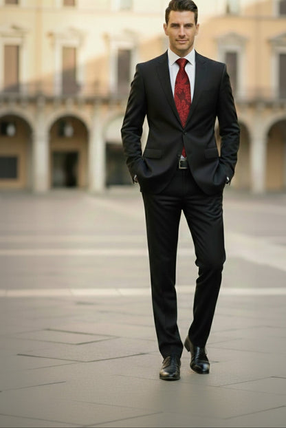 Man in a black suit with a red tie standing in an open square with classical architecture.