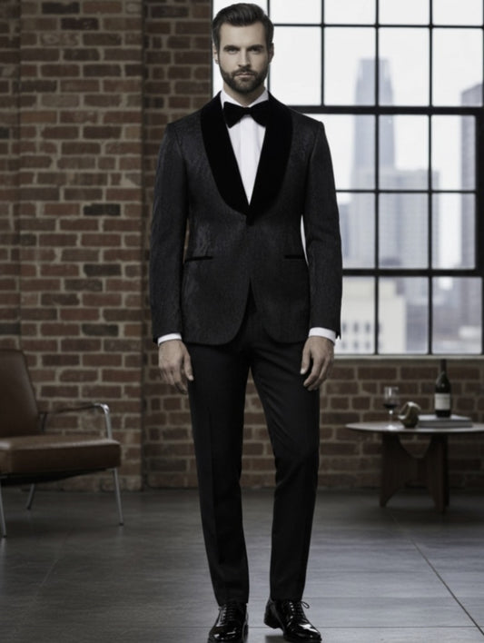 Man in a black tuxedo standing in a room with brick walls and large windows.