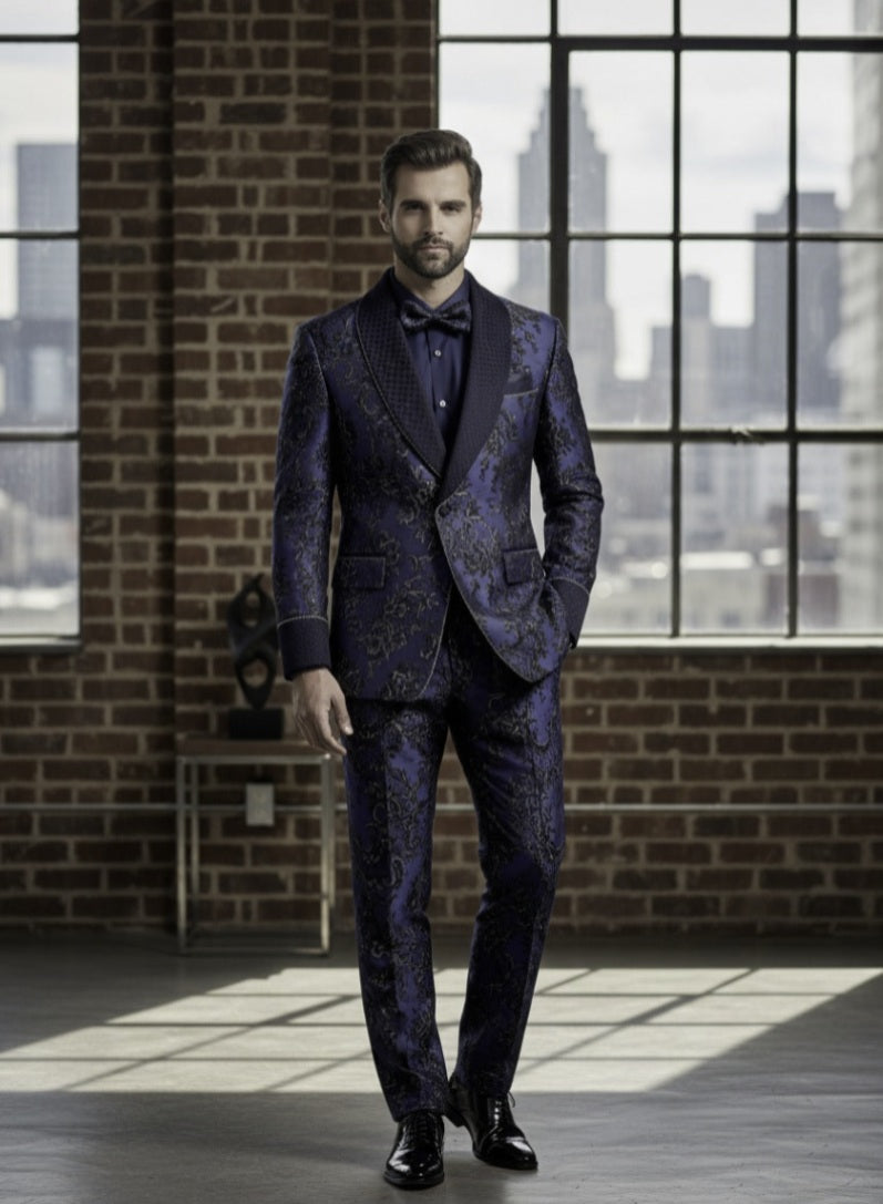 Man in a blue patterned suit standing in a room with large windows and brick walls.