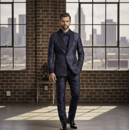 Man in a blue patterned suit standing in a room with large windows and brick walls.