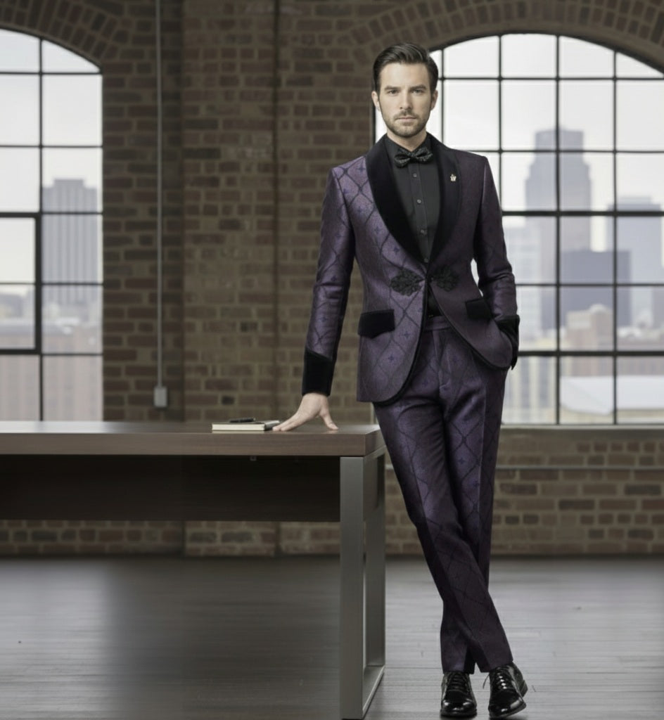 Man in a purple suit with black lapels standing in a room with brick walls and large windows.