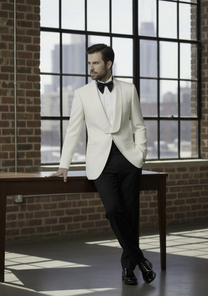 Man in a white tuxedo standing in a room with large windows and brick walls.