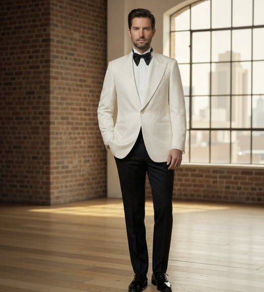 Man_in_a_white_tuxedo_with_black_bow_tie_standing_in_a_room_with_brick_walls_and_large_windows.