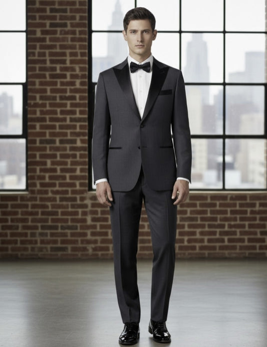 Man wearing a Grey tuxedo standing in front of a large window with a cityscape view.