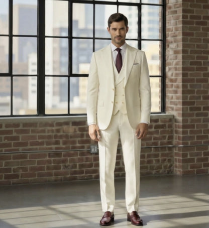 Man wearing a Ivory 3pc suit standing in a room with large windows and brick walls.