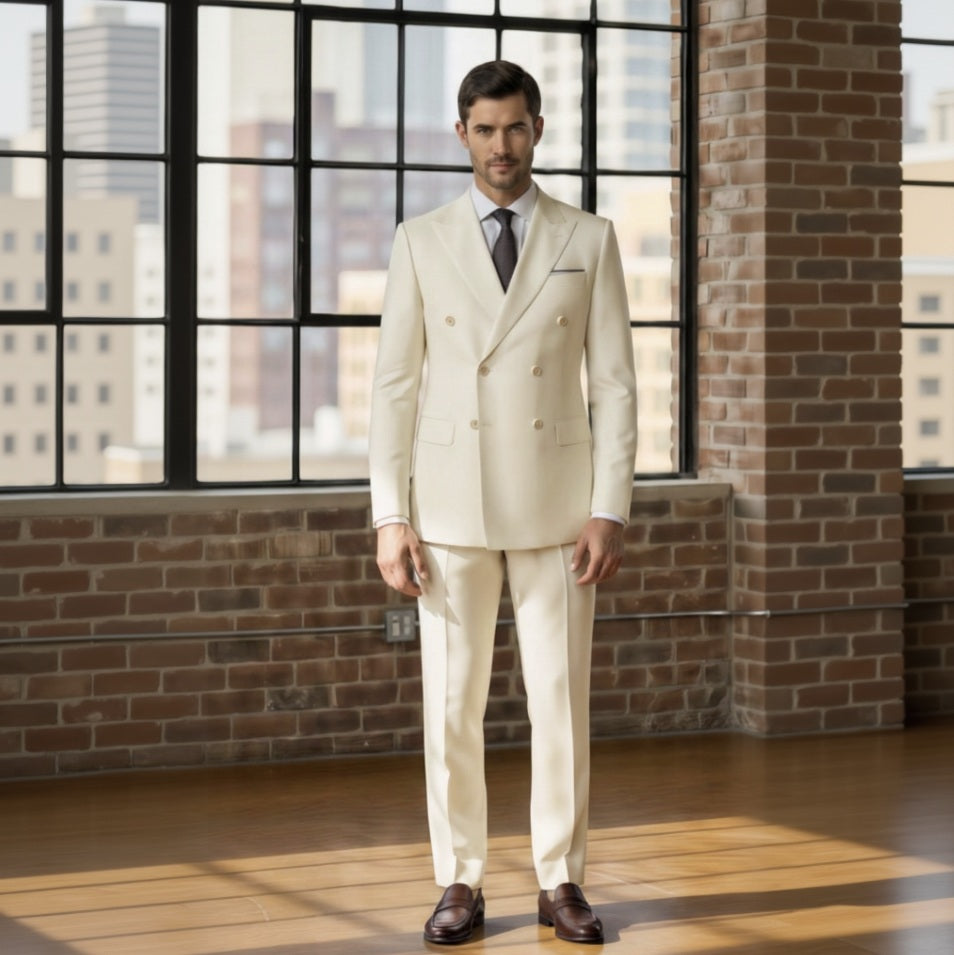 Man wearing a Ivory suit standing in front of a brick wall with large windows.