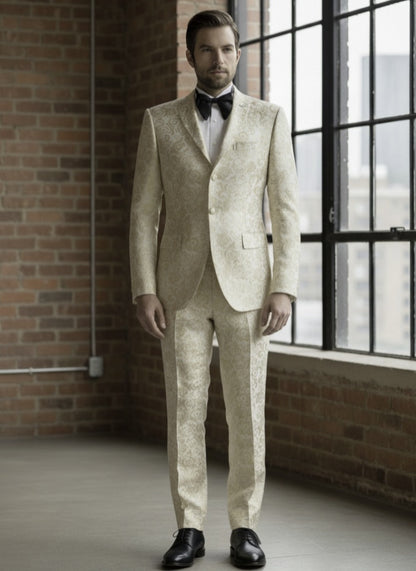 Man wearing a beige suit with a bow tie in an indoor setting with brick walls and large windows.