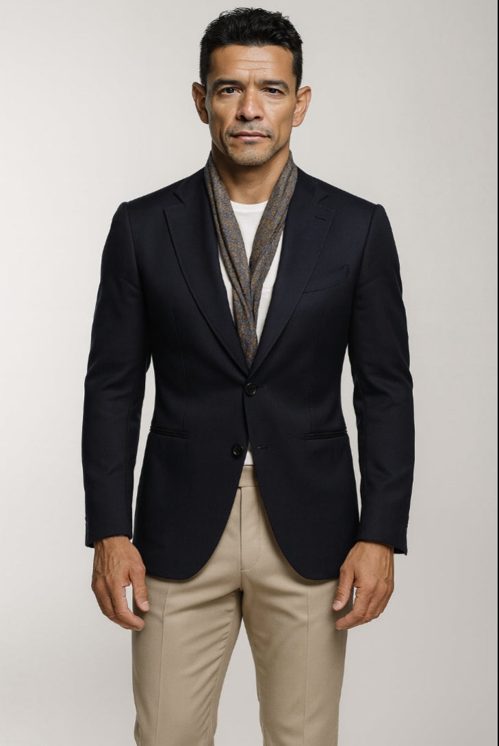 Man wearing a black blazer, white shirt, and beige pants against a plain background