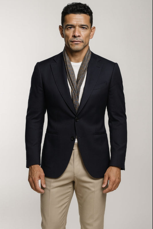 Man wearing a black blazer, white shirt, and beige pants against a plain background