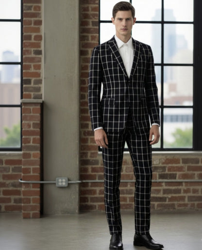 Man wearing a black checkered suit standing in a room with large windows and brick walls.