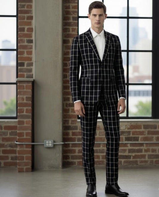 Man wearing a black checkered suit standing in a room with large windows and brick walls.