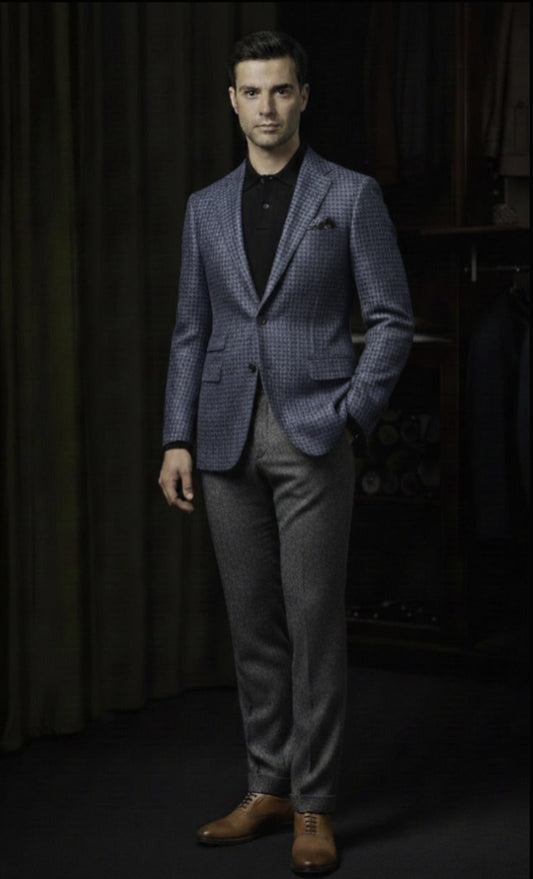 Man wearing a blue checkered blazer and grey pants against a dark background