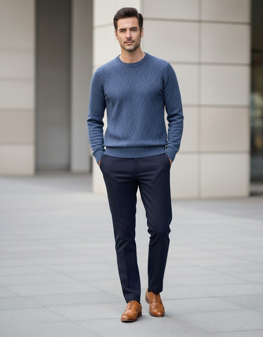 Man wearing a blue sweater, navy pants, and brown shoes standing on a city street.