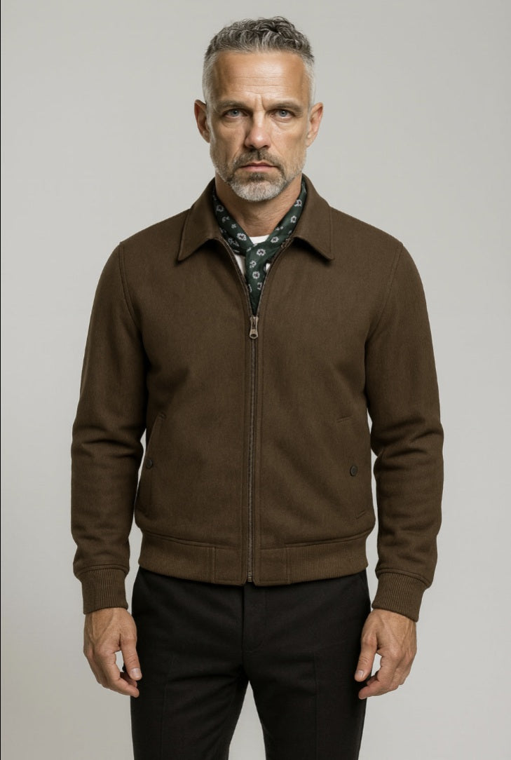 Man wearing a brown jacket over a patterned shirt on a gray background