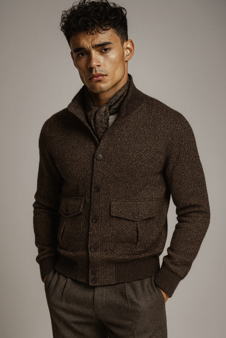 Man wearing a brown textured cardigan over a patterned scarf against a plain background