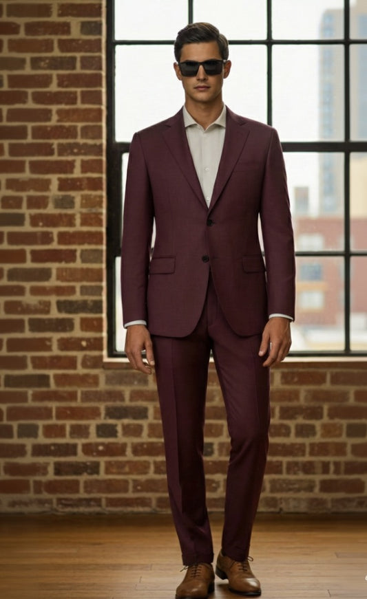 Man wearing a burgundy suit standing in front of a brick wall with large windows.