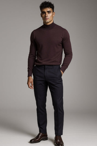 Man wearing a burgundy turtleneck sweater and black pants against a gray background