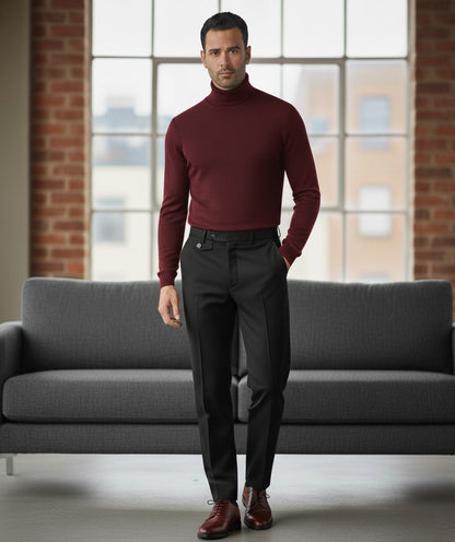 Man wearing a burgundy turtleneck sweater and dark pants standing in a room with a gray couch and large windows.