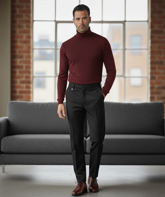 Man wearing a burgundy turtleneck sweater and dark pants standing in a room with a gray couch and large windows.