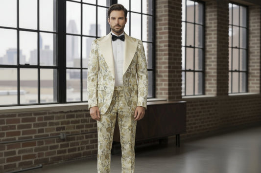 Man wearing a floral suit standing in a room with large windows and brick walls.