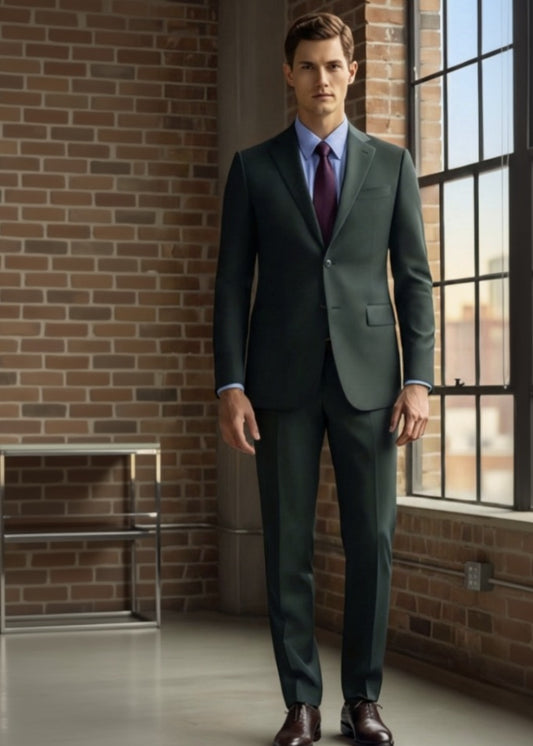 Man wearing a forest green suit standing in a room with brick walls and large windows.