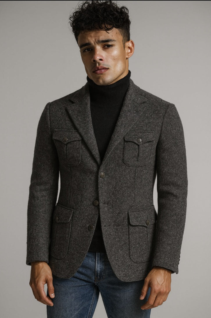 Man wearing a gray blazer over a black turtleneck and jeans against a plain background