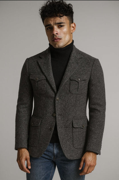 Man wearing a gray blazer over a black turtleneck and jeans against a plain background