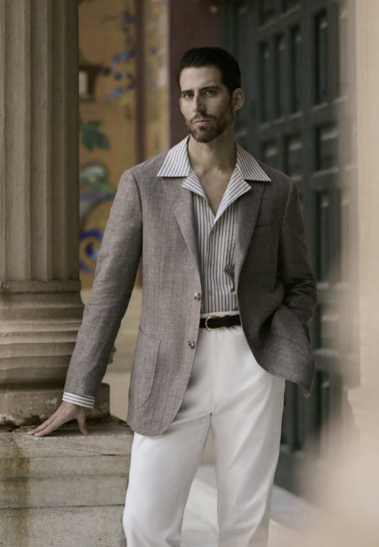 Man wearing a gray blazer, striped shirt, and white pants standing outdoors.
