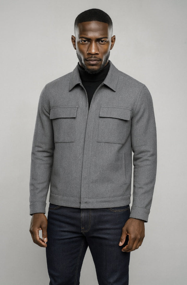 Man wearing a grey jacket and dark jeans against a plain background