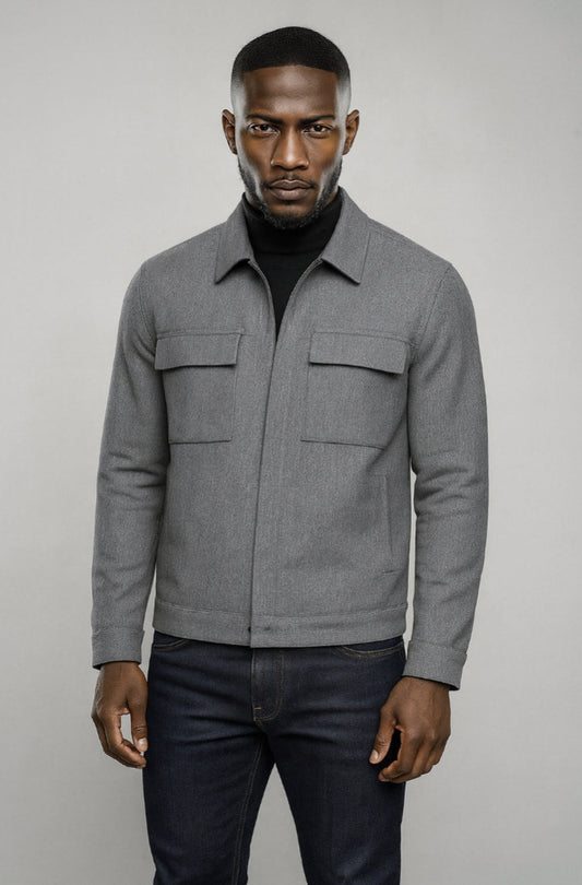 Man wearing a grey jacket and dark jeans against a plain background