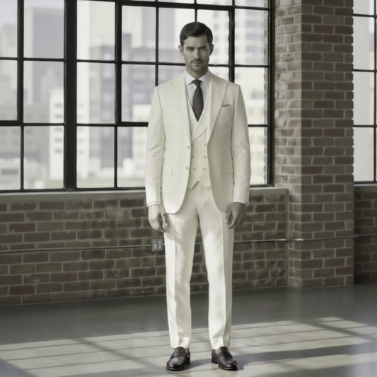 Man wearing a light-colored suit standing in a room with large windows and brick walls.