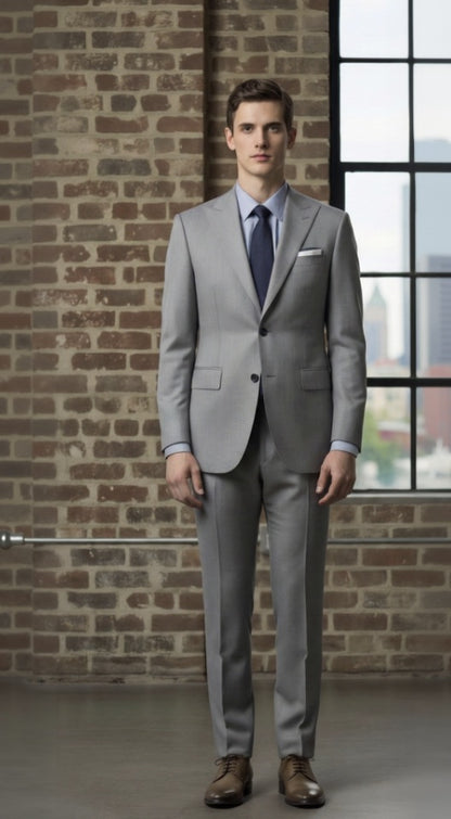 Man wearing a light grey suit standing against a brick wall with a window in the background