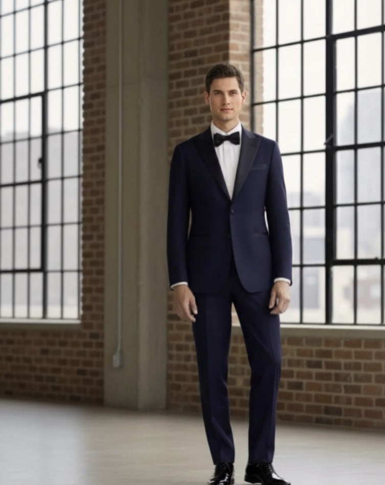 Man wearing a navy blue suit with a bow tie in a room with large windows and brick walls.