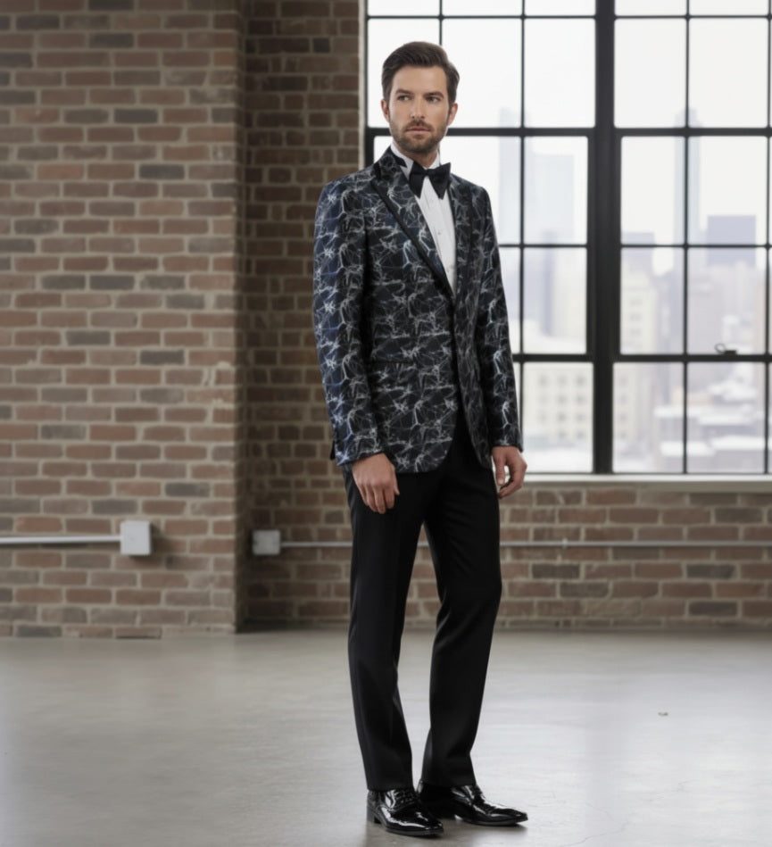 Man_wearing_a_patterned_blazer_and_black_pants_in_an_industrial-style_room_with_brick_walls_and_large_windows