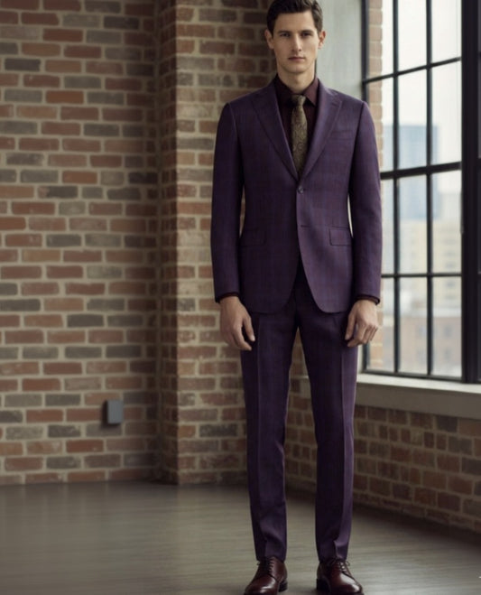 Man wearing a purple check suit standing in front of a brick wall with large windows.