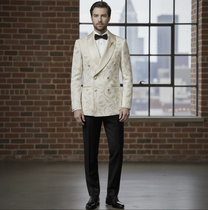 Man wearing a white floral tuxedo with black bow tie and pants, standing in front of a brick wall and window with cityscape view.